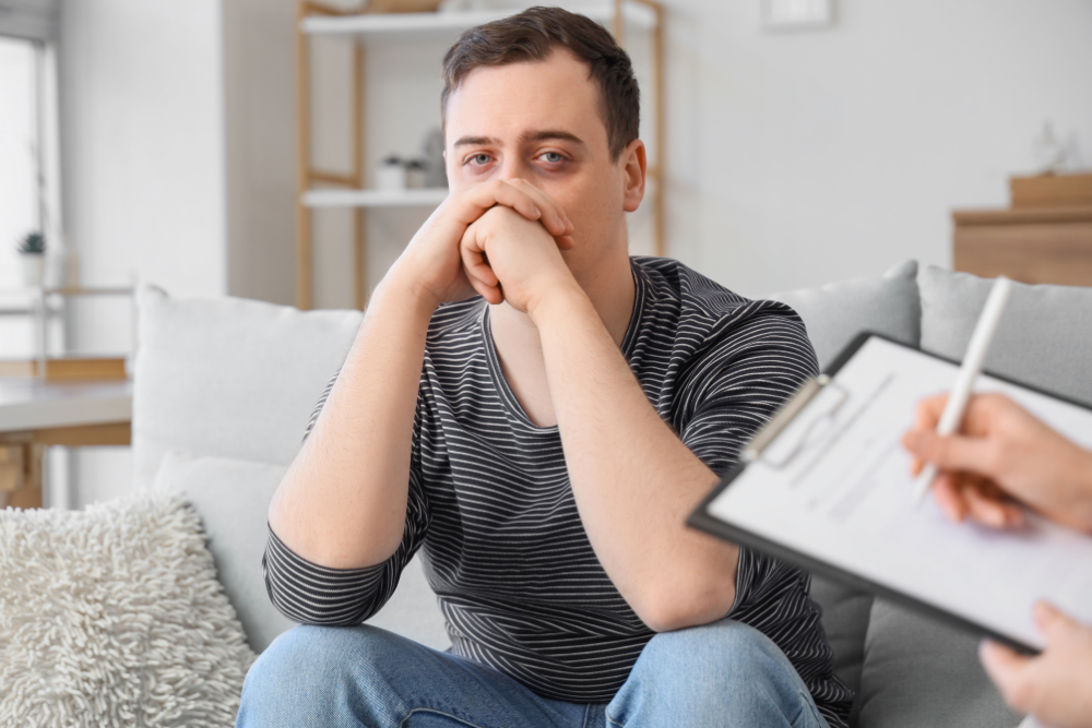 Person holding clipboard with a man on a couch at intake, wondering how long rehab is.