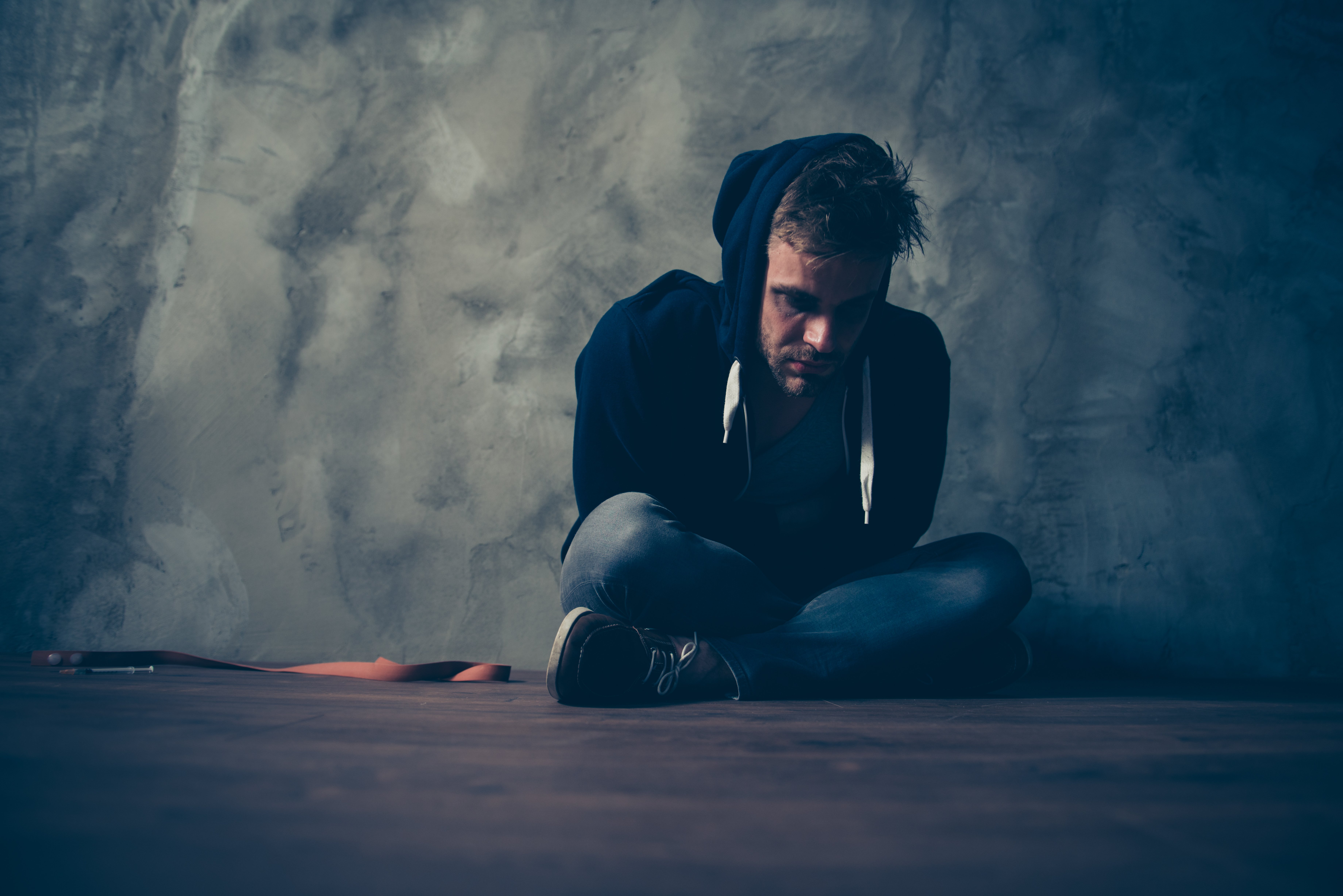 Image of depressed man sitting on floor as Avenues Recovery explores drug abuse hotlines in New Hampshire