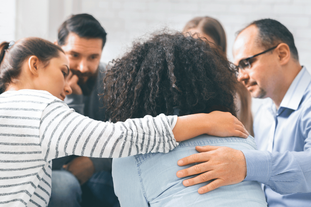 African woman being comforted by friends in Al-anon meeting, discussing her alcoholic spouse