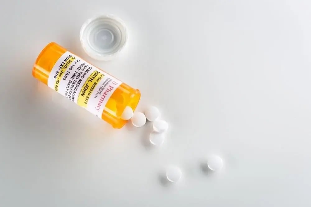 Alcoholism medication pills spill from an open bottle on a white surface