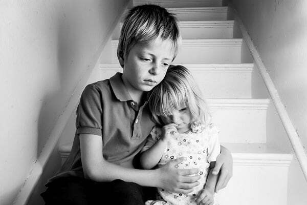 Brother holding his frightened younger sister, symbolizing foster care trauma and its link to later addiction.