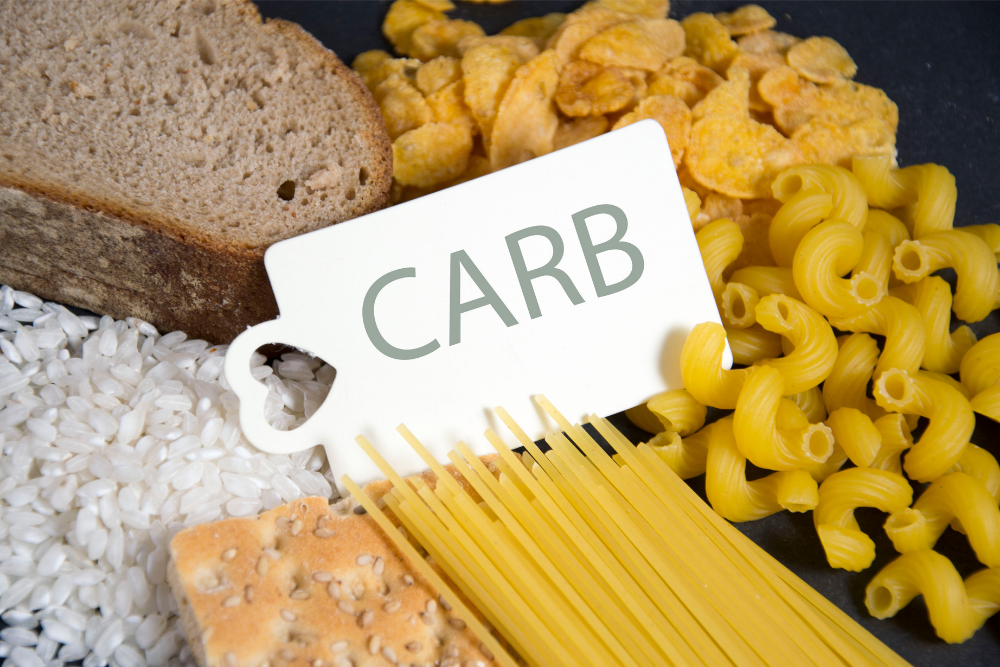 "Carb" sign surrounded by whole-grain bread, pasta, and cereal, key to having energy in recovery