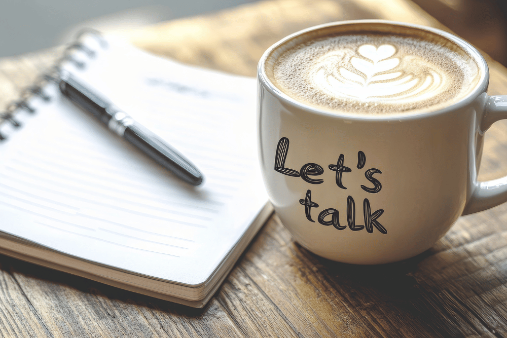 Coffee mug labeled “let’s talk” beside a notebook and pen. Avenues Recovery advises an open conversation