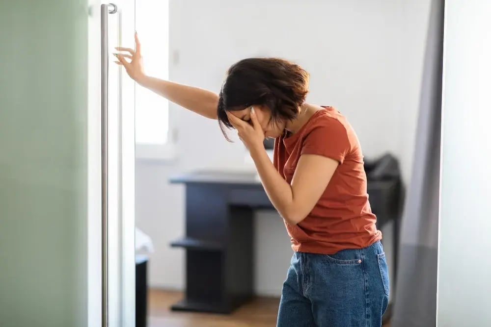 A woman holding her face and leaning over in dizziness, a symptom caused by drinking isopropanol.