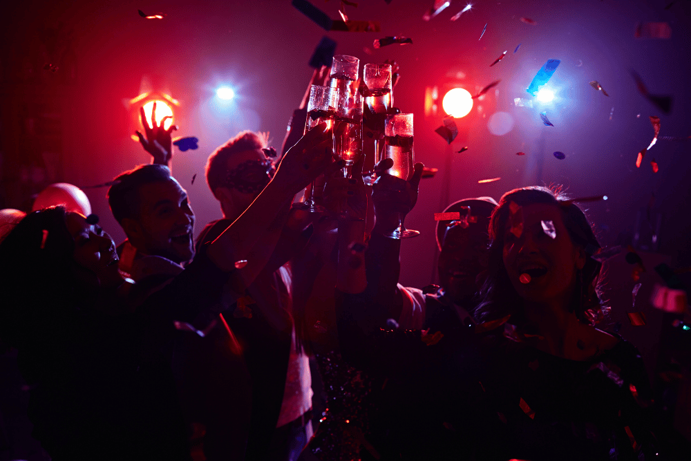 Friends gathered together, clinking glasses of alcohol in a party with disco lights
