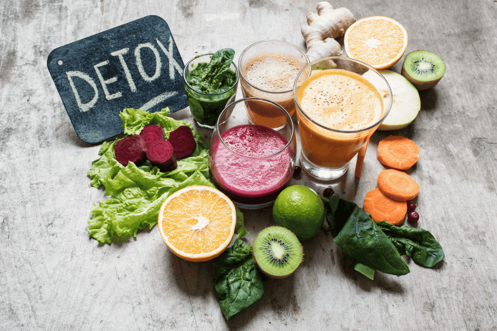 Glasses with assorted drinks surrounded by fruits and vegetables, illustrating the ingredients in drug detox drinks.
