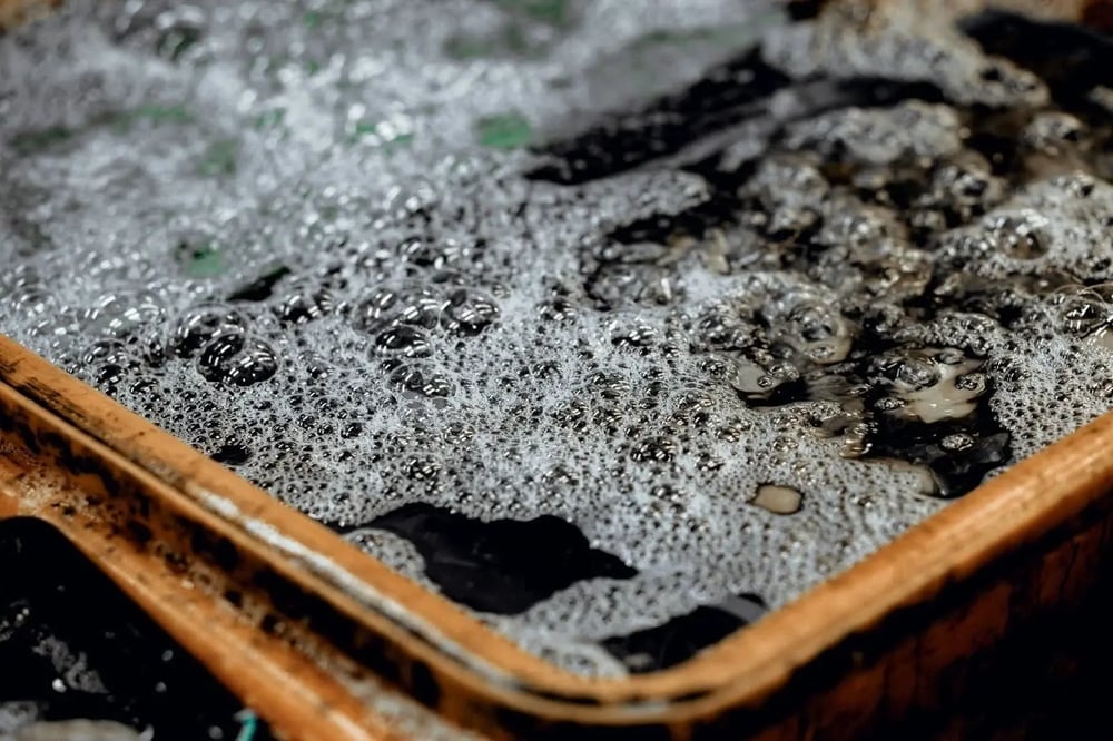 Coca leaves submerged in a tub of gasoline, with white bubbles forming on the top.