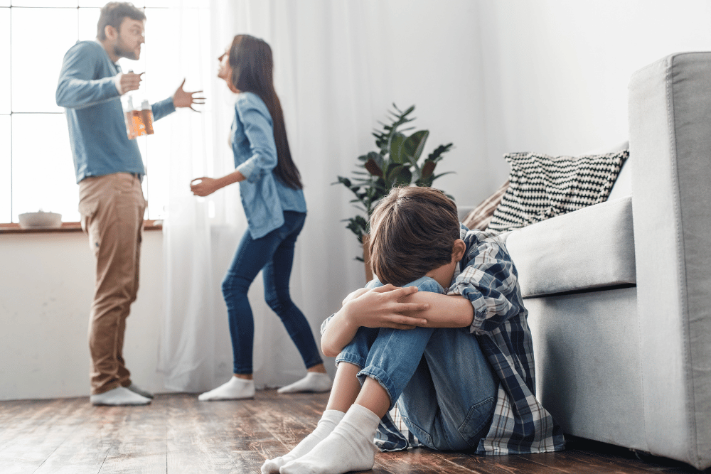 Couple arguing, husband holding whiskey bottle, while son sits on floor, head in his knees