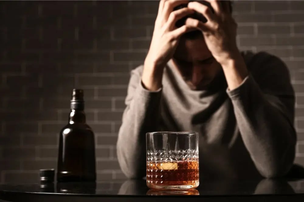 Man clutching his head, with a glass of whiskey he hopes is a quick-fix for insomnia.