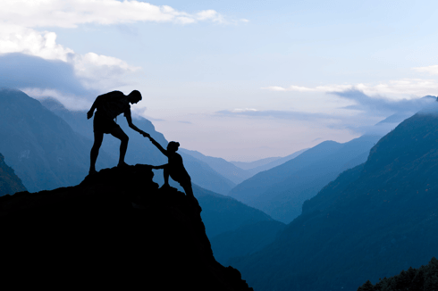 Friend-Helping-Friend-Climb-To-Peak-Of-Hill