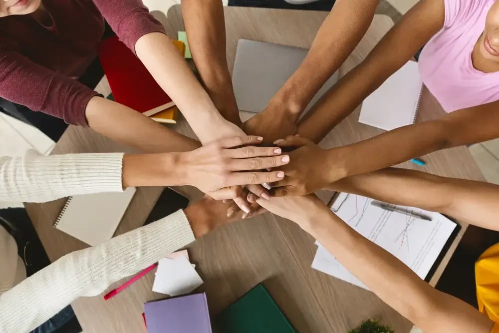 Several hands joining over a table, symbolizing the unity and support fostered during National Recovery Month.