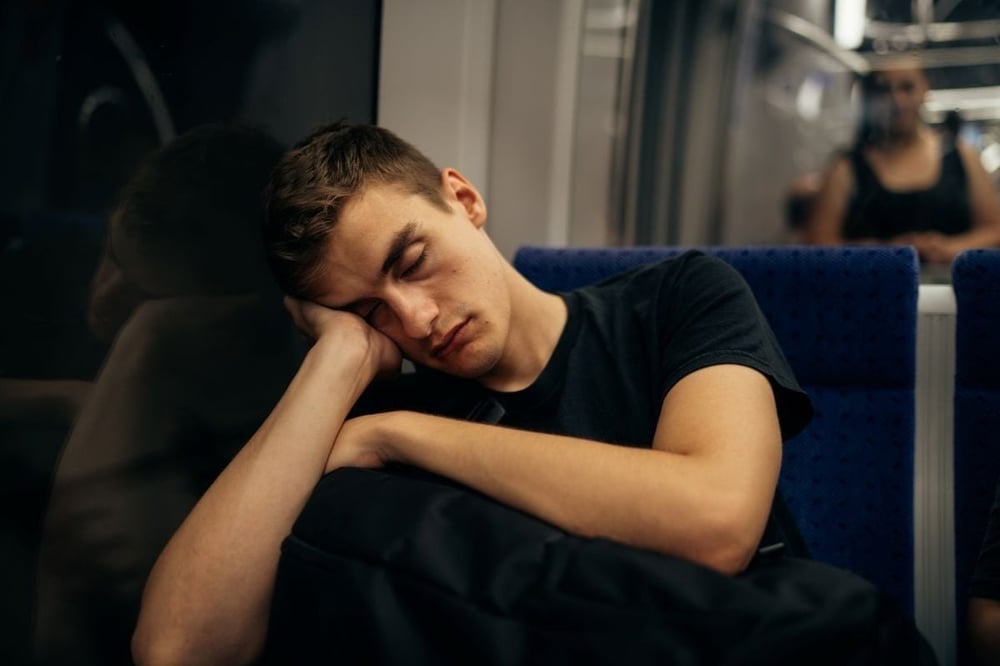 A man sitting, his face leaning on his hand, eyes closed. Fatigue: a symptom of dehydration.