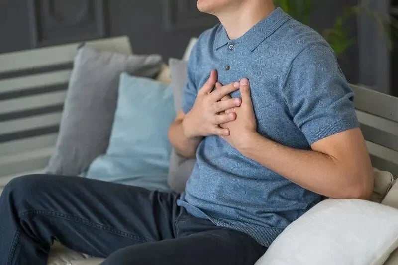 Man sitting on seat with hands on chest, experiencing chest pain after drinking alcohol