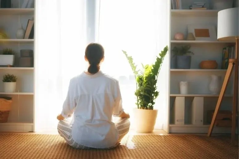 A woman sits cross-legged on a floor mat, practicing meditation during holistic addiction treatment