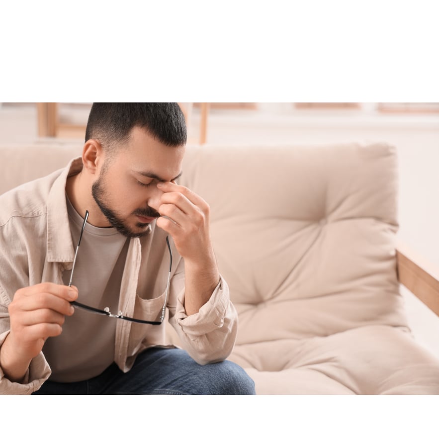 Man sitting on couch with eyes closed and face pained, experiencing trazodone overdose symptoms.