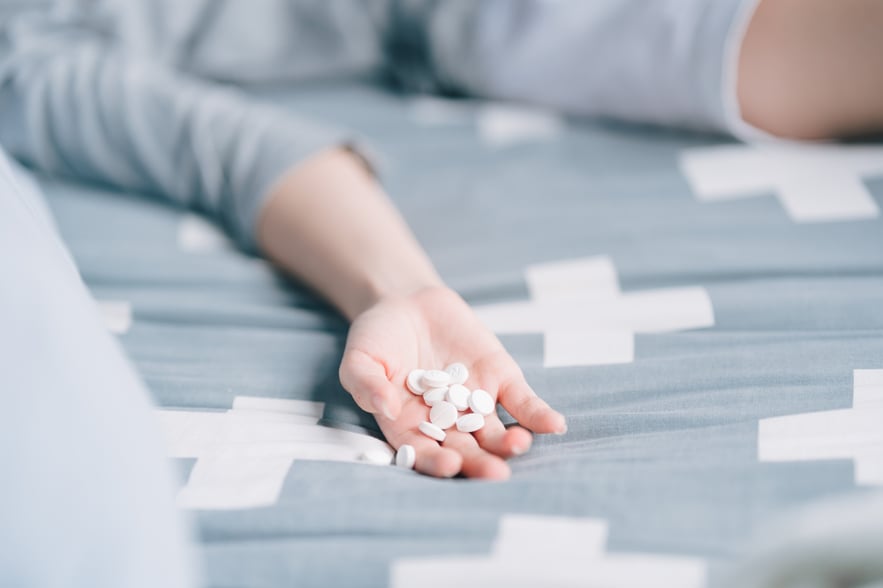 Hand holding several white tablets on a bed, depicting the potential signs of a Percocet overdose.