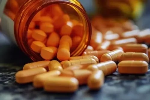 Medicine similar to Adderall spills from an open medication bottle on a countertop.