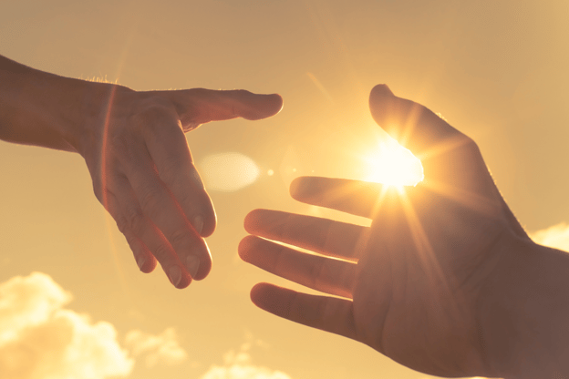 Hands meeting in warm sunlight, illustrating how to help an addict by reaching out a hand