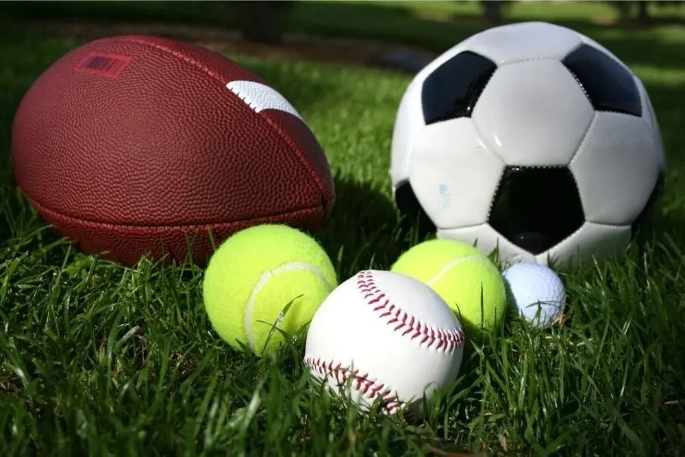 Various sports balls on grass, illustrating fun sober activities like practicing sports and staying active outdoors