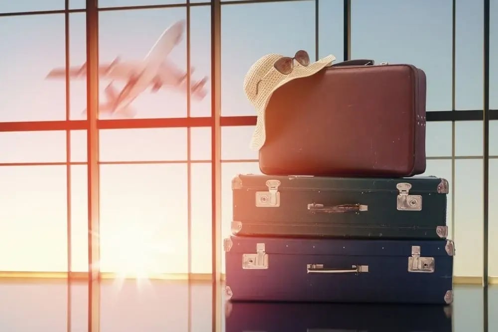 Stacked suitcases, sun hat, and sunglasses by airport window, representing enjoyable sober activities like traveling