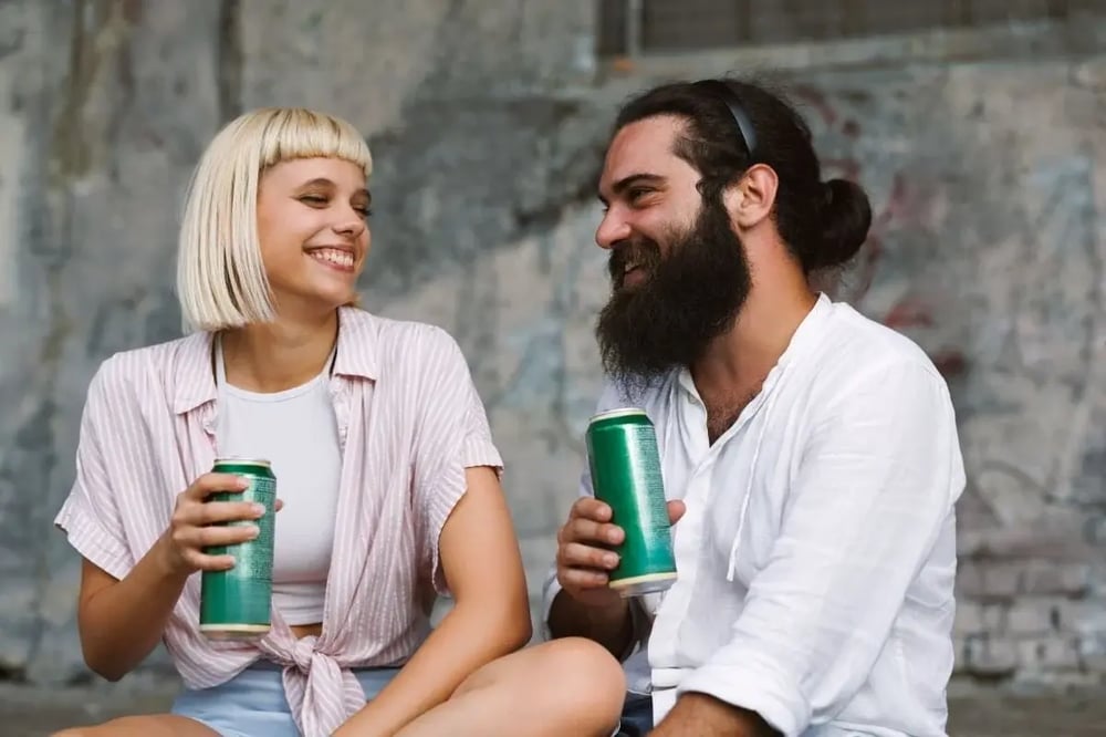 Two friends holding canned drinks and chatting outdoors on a warm summer day.