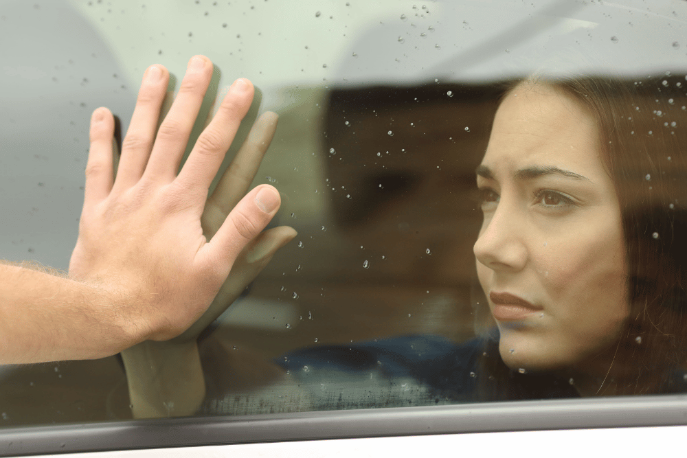 Woman placing her hand on the car window, against her relative’s hand, saying goodbye to them