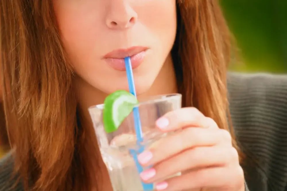 A woman sipping water from a glass with a straw. Sipping water frequently rehydrates after drinking.