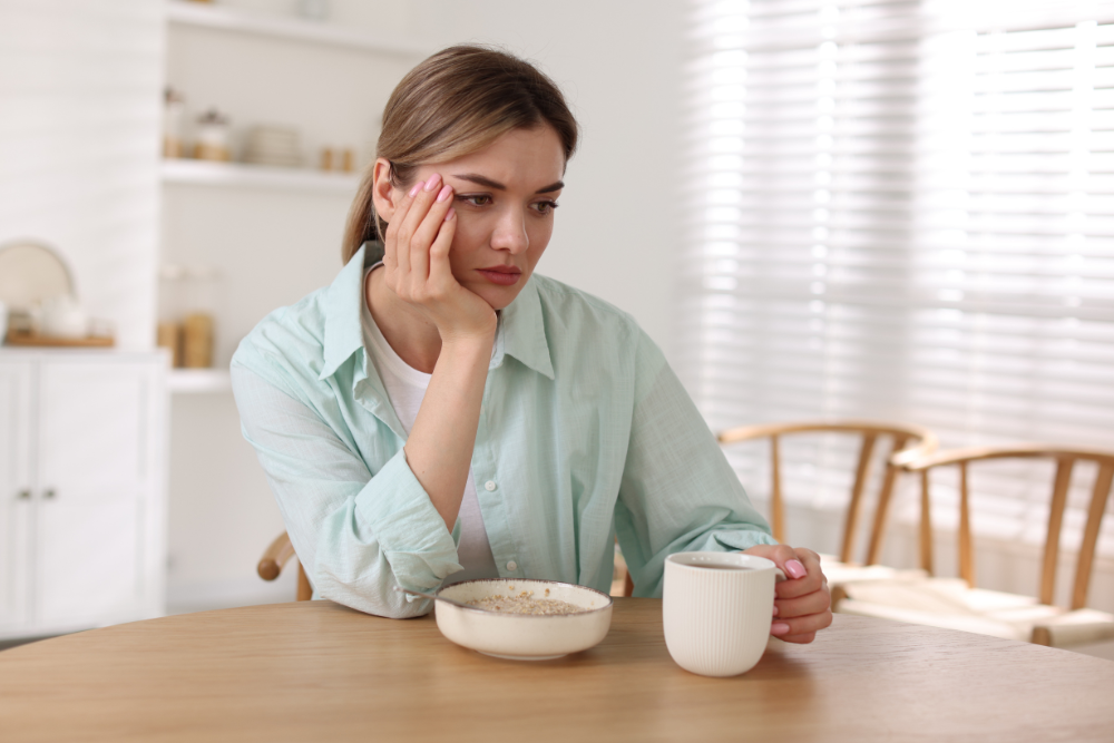 Woman looking troubled, staring past her uneaten oatmeal, illustrating loss of appetite after recently starting Adderall.