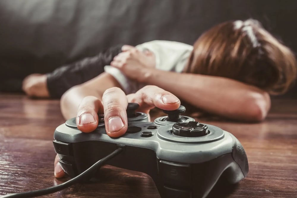 Young man lying face down on a wooden floor, his hand resting on a gaming pad.