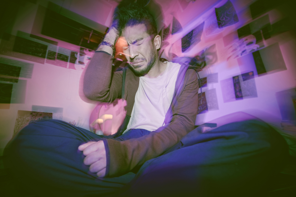 Man clutching head, experiencing confusion, anxiety, and hallucinations from Vyvanse overdose. Avenues Recovery