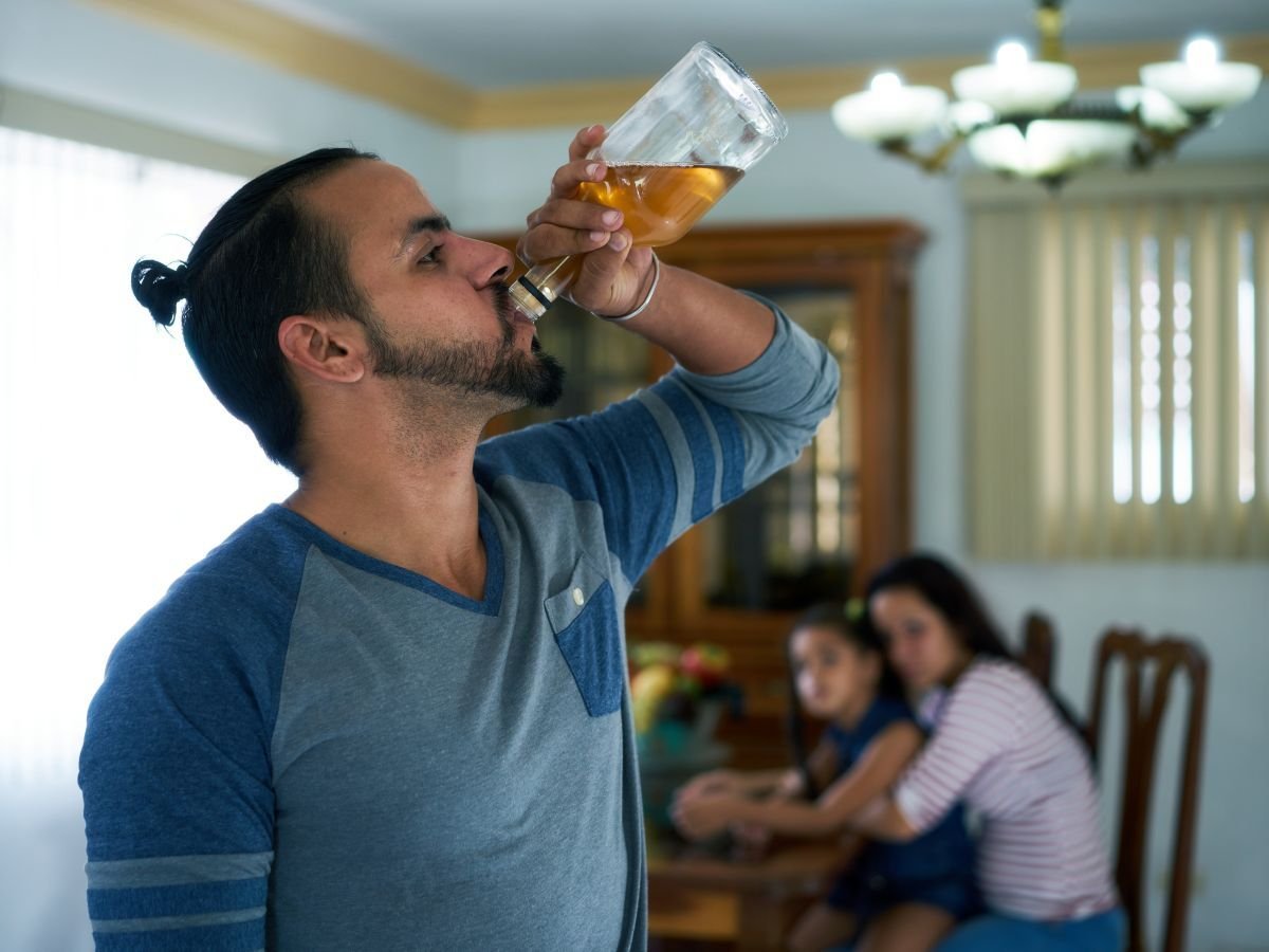 Image of man drinking with frightened wife and child watching as Avenues Recovery explores when to walk away from an addict
