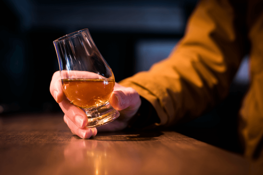 close-up of man holding whisky glass at bar table.