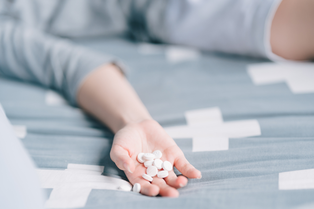 Man collapsed in bed from a Wellbutrin overdose, pills spilling from his hand. Avenues Recovery
