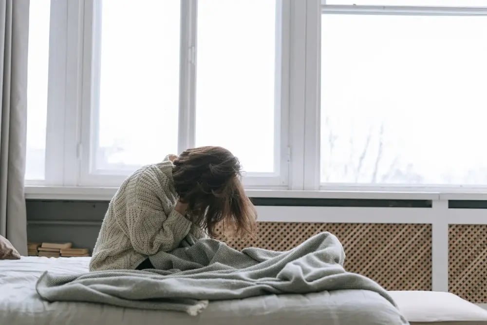 woman sitting in bed with head in hands, experiencing wet brain symptoms