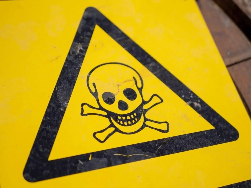 yellow sign showing black skull-and-bones inside triangle as indication of danger.