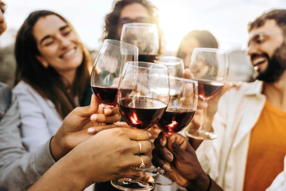 Adults toasting with wine glasses, unaware of the link between alcohol and cancer risk. Avenues Recovery